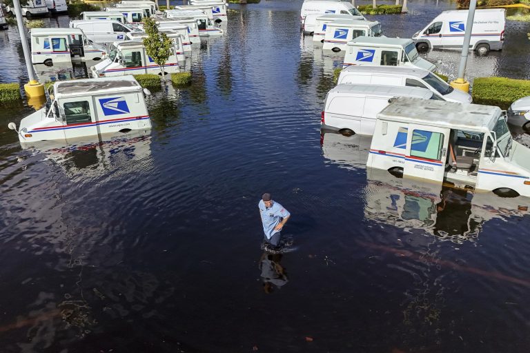 A USPS worker inspects trucks on Friday that had been relocated to protect them from wind but are now underwater due to intense rain from Hurricane Milton in New Port Richey, Fla. (AP Photo/Mike Carlson)