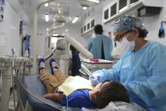 A dentist cleans the teeth of a child in the public health department's mobile dental clinic visiting Starmount Elementary school in Charlotte, N.C., on March 20, 2025. (AP Photo/Mary Conlon)