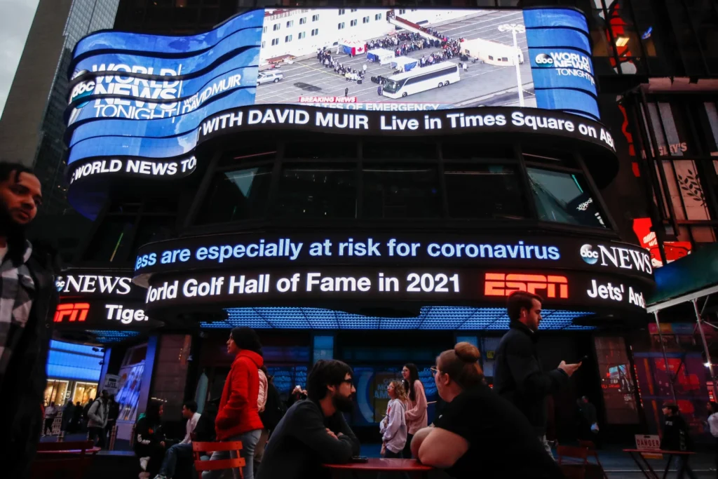 Pedestrians pass under a news ticker in Times Square on March 11, 2020, in New York. (AP Photo/John Minchillo, File)