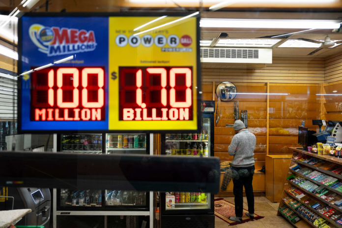 A convenience store employee prays while Jackpot payouts for Powerball and Mega Millions are displayed outside the store, Tuesday, Dec. 23, 2025, in New York. (AP Photo/Yuki Iwamura) Link Copied