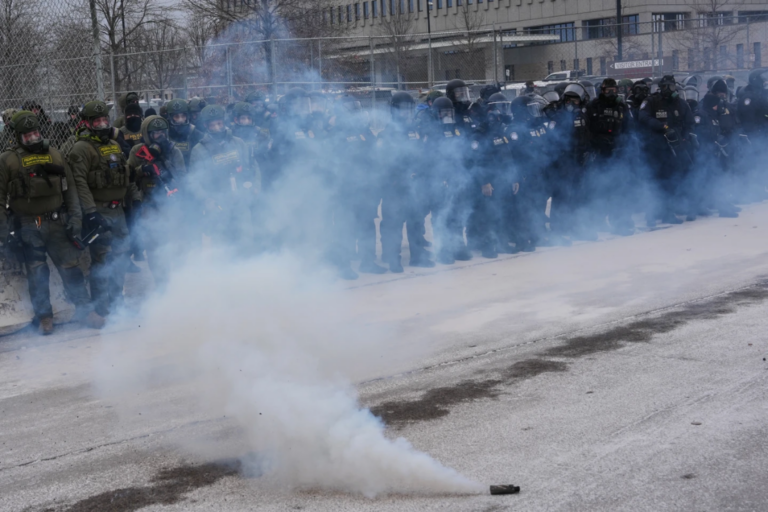 Federal immigration officers stand outside Bishop Henry Whipple Federal Building as tear gas is deployed Thursday, Jan. 15, 2026, in Minneapolis. (AP Photo/Adam Gray)