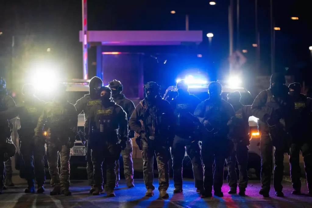 Federal officers stand guard after detaining people outside of Bishop Henry Whipple Federal Building, Tuesday, Jan. 13, 2026, in Minneapolis. (AP Photo/Adam Gray)