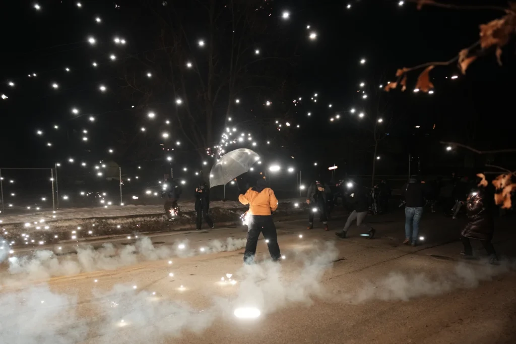 A protester holds an umbrella as sparks fly from a flash bang deployed by law enforcement on Wednesday, Jan. 14, 2026, in Minneapolis. (AP Photo/Adam Gray)

