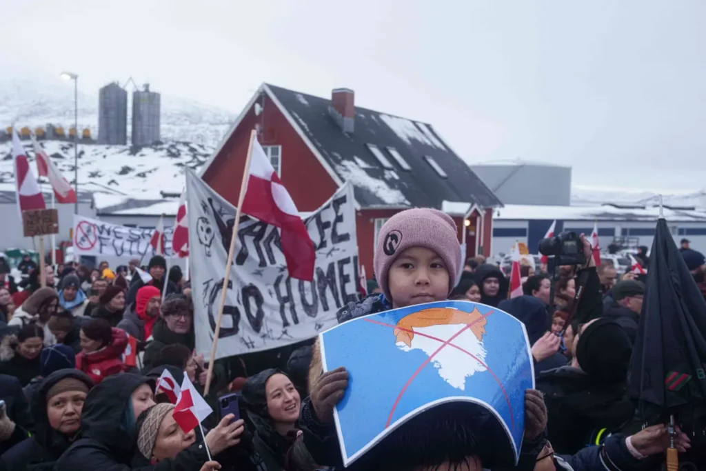 A boy holds a crossed out map of Greenland topped by a hairpiece symbolizing U.S. President Donald Trump, during a protest against Trump's policy towards Greenland in front of the US consulate in Nuuk, Greenland, Saturday, Jan. 17, 2026. (AP Photo/Evgeniy Maloletka) 6 of 7 | A boy holds a crossed out map of Greenland topped by a hairpiece symbolizing U.S. President Donald Trump, during a protest against Trump’s policy towards Greenland in front of the US consulate in Nuuk, Greenland, Saturday, Jan. 17, 2026. (AP Photo/Evgeniy Maloletka)