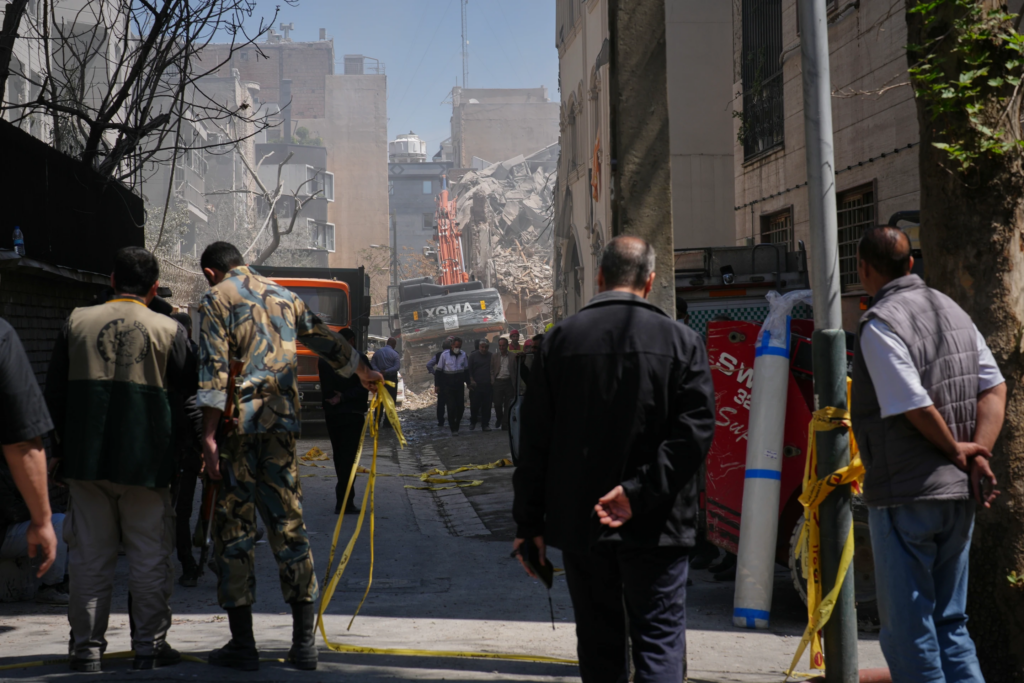 Bystanders watch from a distance as rescue teams and first responders work at the site of a strike that, according to a security official at the scene, destroyed half of the Khorasaniha Synagogue and nearby residential buildings in Tehran, Iran, Tuesday, April 7, 2026. (AP Photo/Francisco Seco). 
