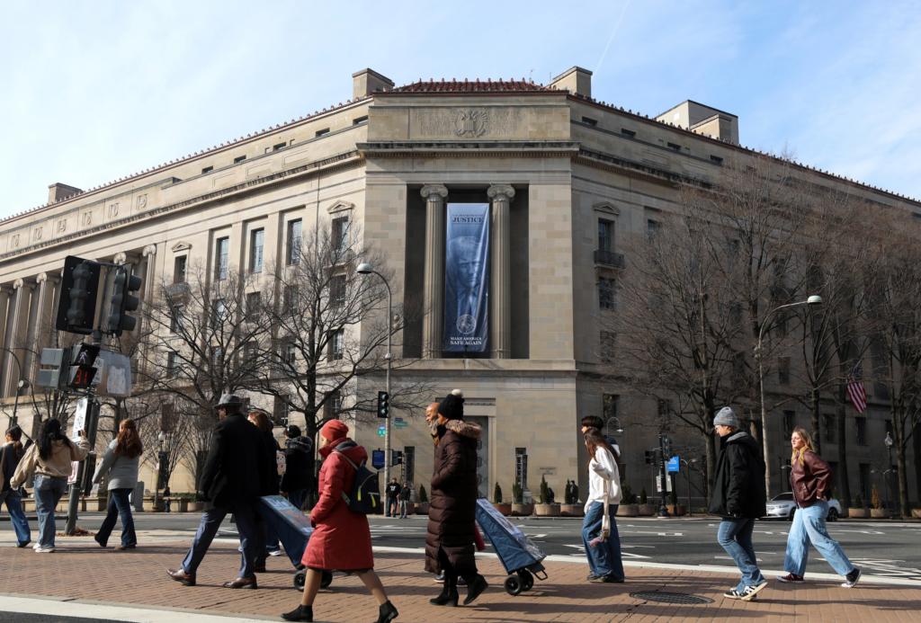 Tourists walk past a banner with President Donald Trump hanging on the Department of Justice, Feb. 27, 2026, in Washington. (AP Photo/Rahmat Gul, File)

