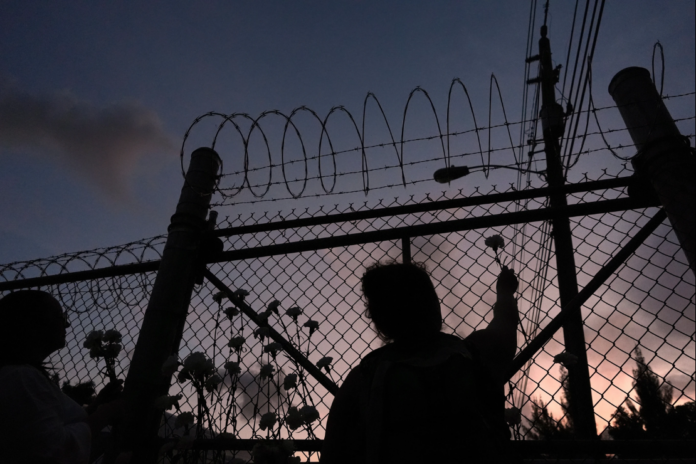 People place flowers on a fence outside Krome Detention Center in Miami, Saturday, May 24, 2025, during a vigil to recognize people who have died in U.S. Immigration and Customs Enforcement custody as well as those affected by mass deportations. (AP Photo/Rebecca Blackwell, File)