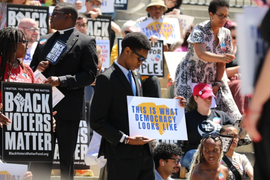 A protestor stands outside the South Carolina Statehouse on Thursday, May 14, 2026, in Columbia, S.C. (AP Photo/Jeffrey Collins)
