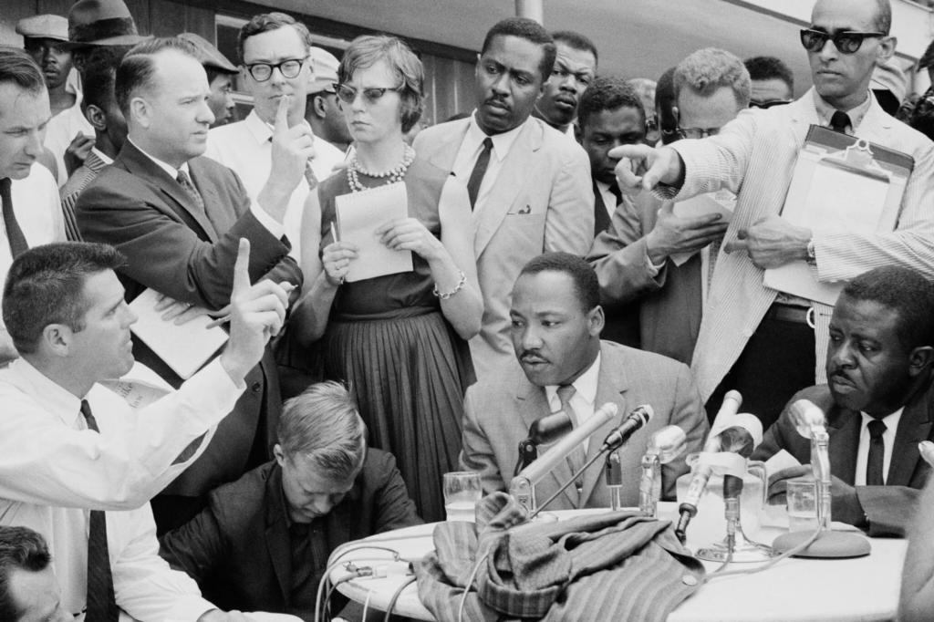 As the Rev. Dr. Martin Luther King Jr., seated, speaks to the press in Birmingham, Ala., in 1963, Mr. Jones stands behind him. Credit. Ernst Haas/Hulton Archive/Getty Images