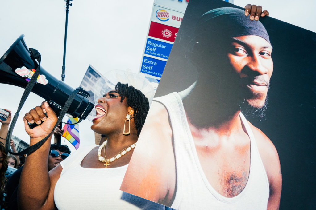Qween Jean, the founder of the advocacy group Black Trans Liberation, spoke while holding a photograph of O’Shae Sibley at a Mobil gas station in Brooklyn on Friday. Credit:Jutharat Pinyodoonyachet for The New York Times