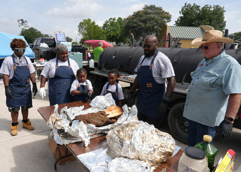 he Loving family and pitmaster Larry Zimmerman examine an overnight-smoked Watusi shoulder during the 11th Annual Community Junior Chef Competition at Mission County Park on July 18, 2026. Team Loving won the competition. (Photo by Burrell Parmer)