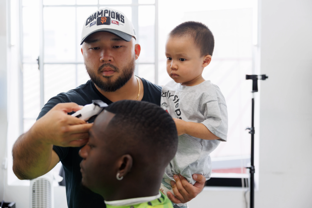 Jack Chang cuts Isaac Obamehinti’s hair while holding his 2-year-old son Cairo Miu at his studio on Monday, July 13, 2026, in San Francisco. (AP Photo/Juliana Yamada)